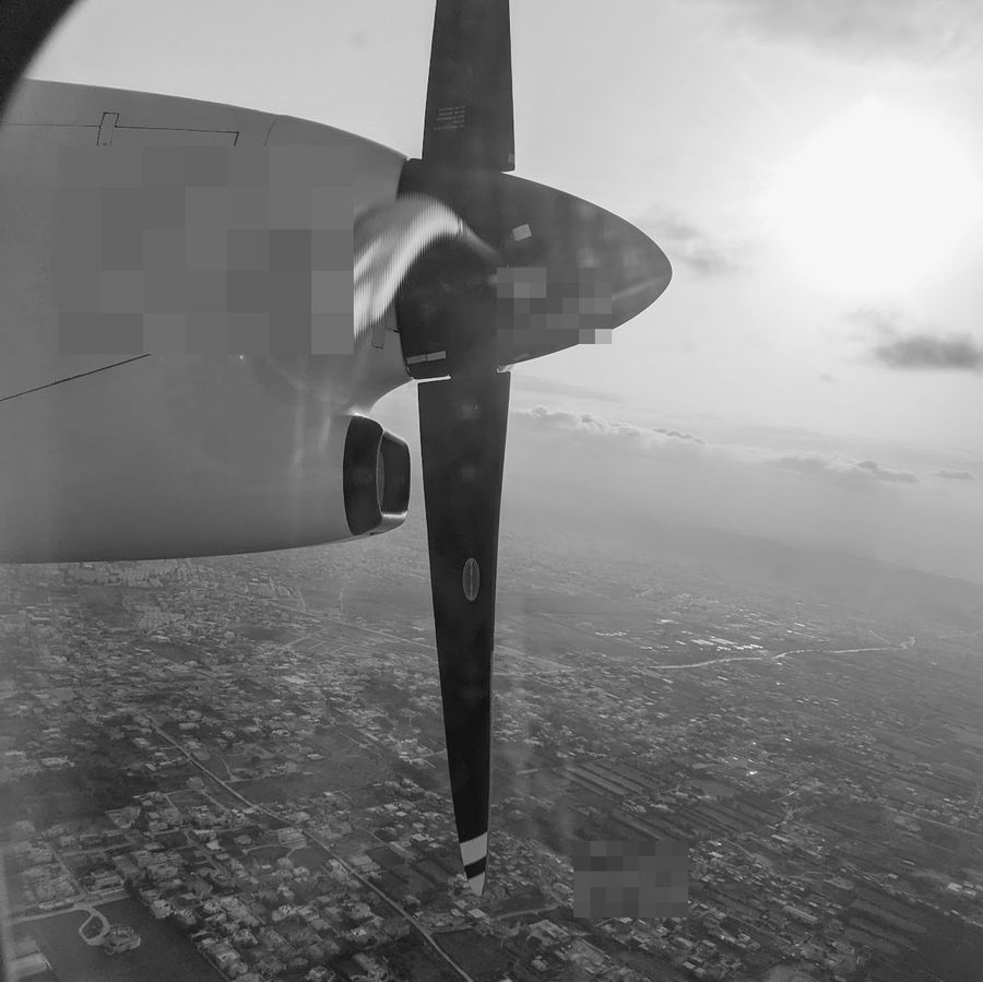 A turboprop wing and propeller over a city on approach.
