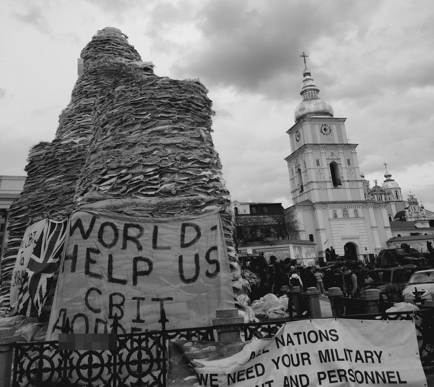 A monument encased in sandbags, a cathedral behind it.